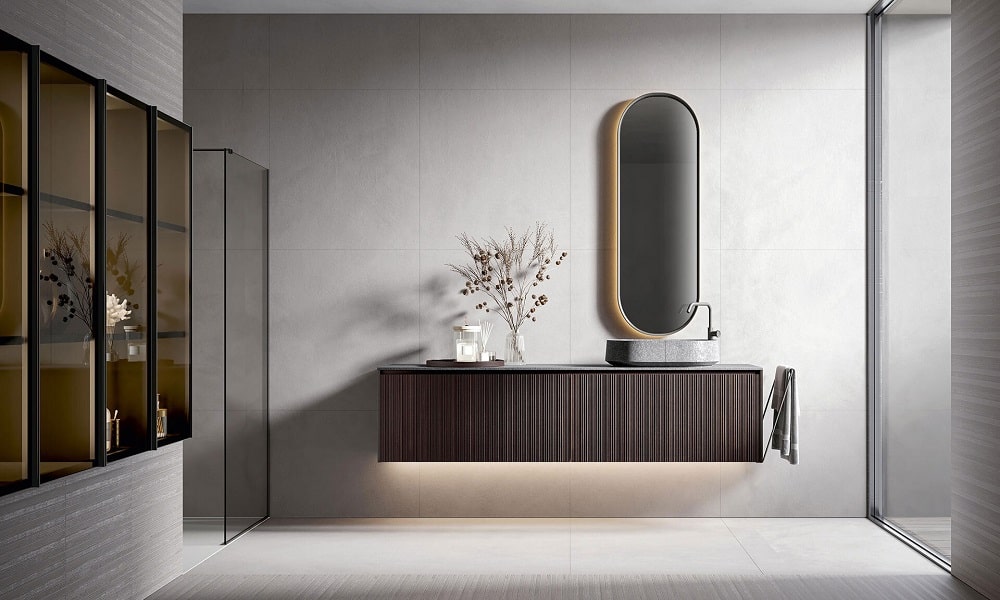 Modern bathroom vanity with floating wood cabinetry, integrated stone basin, oval backlit mirror, minimalist faucet, large-format porcelain tiles, and glass shower enclosure in a contemporary luxury bathroom design.