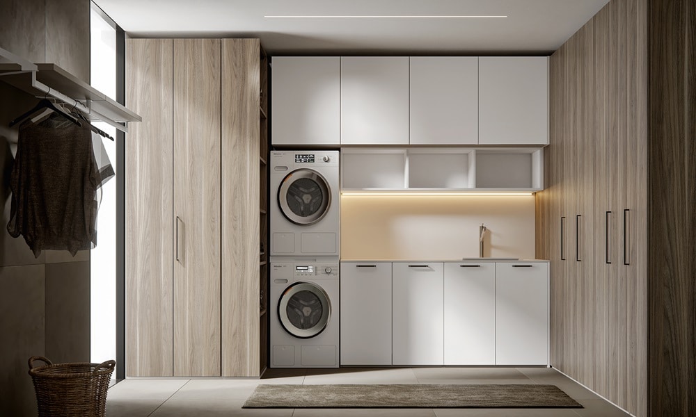 Modern laundry room with integrated washer and dryer, white cabinetry, warm wood panels, concealed storage, and soft under-cabinet lighting in a clean, minimalist design.