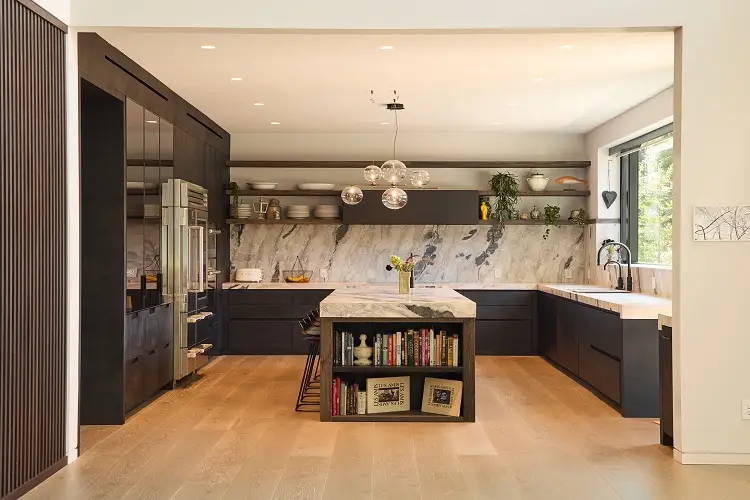 Elegant modern kitchen with dark cabinetry, marble backsplash and island, open shelving with decor, integrated appliances, warm wood flooring, and soft ambient lighting in a spacious layout.