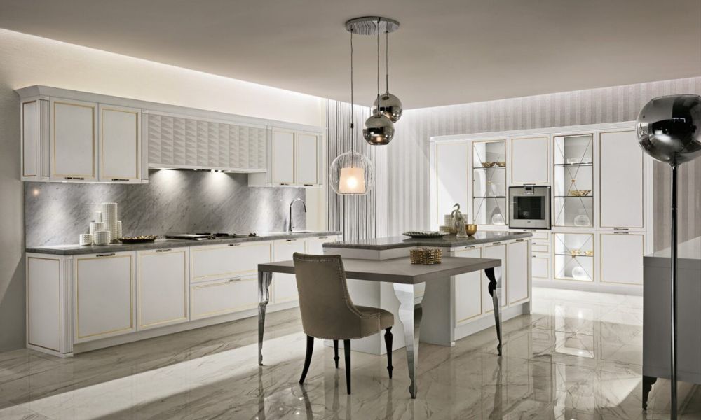 Luxury Glam kitchen by Aster Cucine featuring elegant white cabinetry with gold accents, marble countertops, glass display cabinets, and sophisticated lighting.