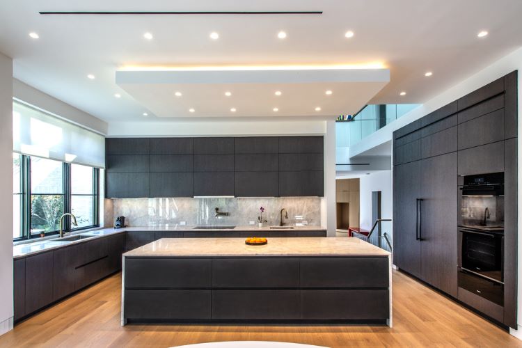 Contemporary dark wood kitchen in Tenafly, NJ with custom cabinetry, large stone island, and integrated appliances.