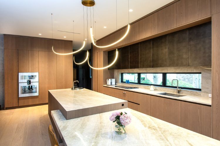 Modern wood kitchen in Cresskill, New Jersey with custom cabinetry, stone island, integrated appliances, and sculptural pendant lighting.