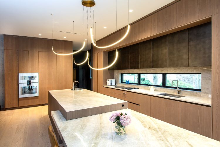 Modern wood kitchen in Cresskill, New Jersey with custom cabinetry, stone island, integrated appliances, and sculptural pendant lighting.
