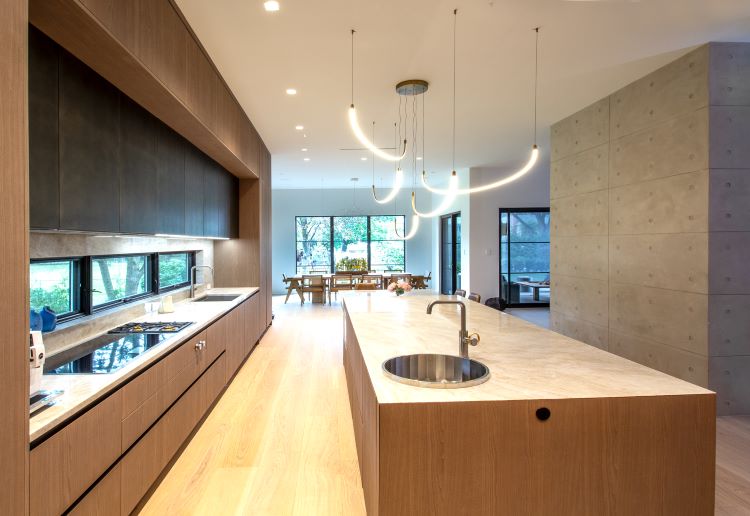 Modern luxury kitchen with warm wood cabinetry, custom European cabinets, marble island, integrated appliances, and contemporary pendant lighting in a high-end residential interior